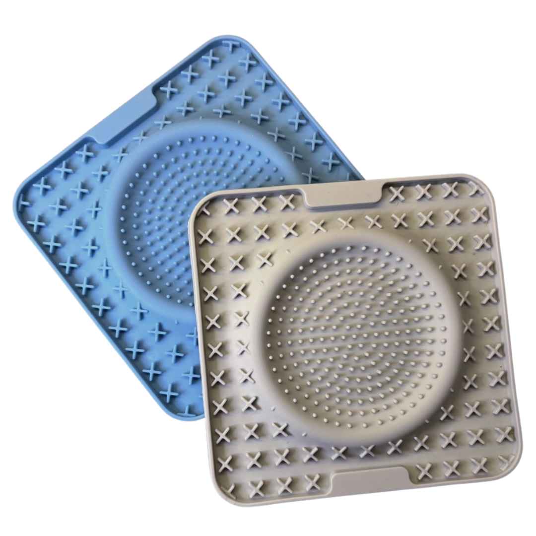 Two square lick mats, one in blue and the other in grey, featuring a circular pattern of raised bumps in the center and an outer border of X-shaped raised elements for added texture and stimulation